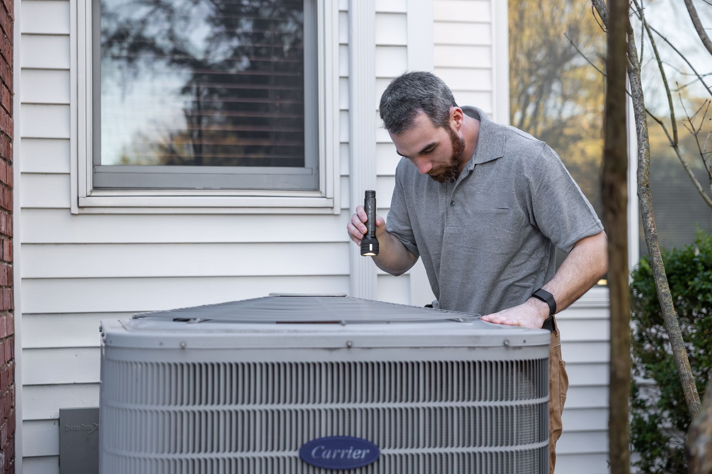 Technician inspecting a Carrier condenser beside a house